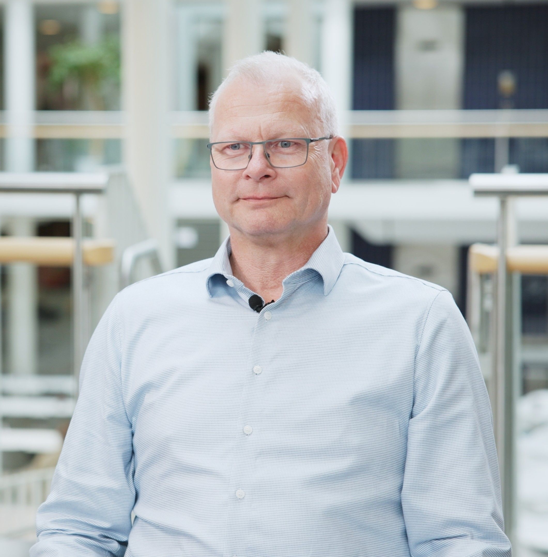 Ulrich Bernhardt in hellblauem Hemd mit Ansteckmikrofon, stehend in einem Bürofoyer