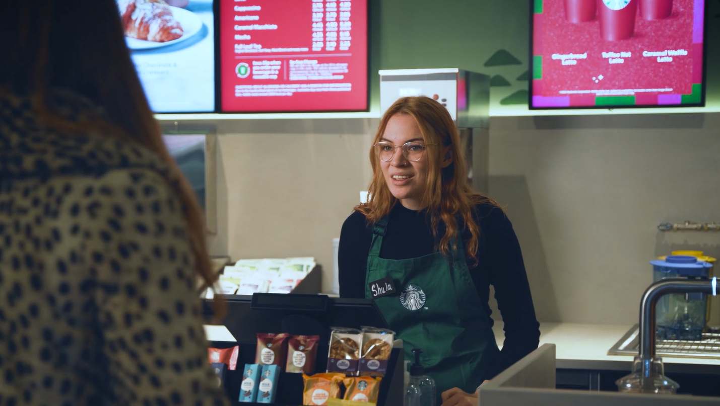 Starbucks-Barista in grüner Schürze bedient einen Gast an der Theke