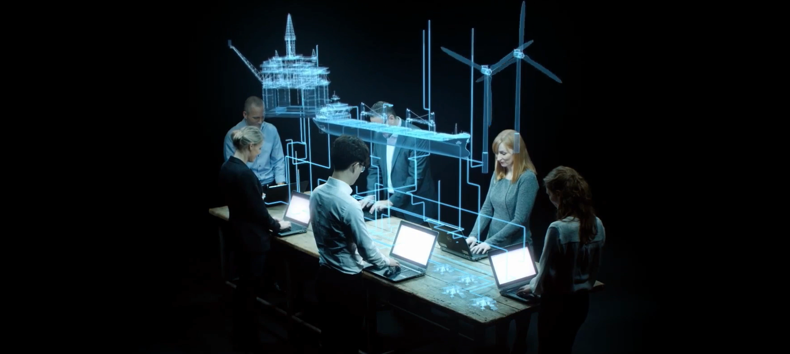 Team an Laptops rund um einen Tisch, darüber holografische Drahtgittermodelle einer Offshore-Plattform, eines Schiffs und einer Windturbine