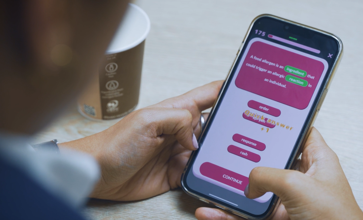 Nahaufnahme von Händen, die ein Smartphone mit einer Lückentext-Quizfrage zu Lebensmittelallergenen halten