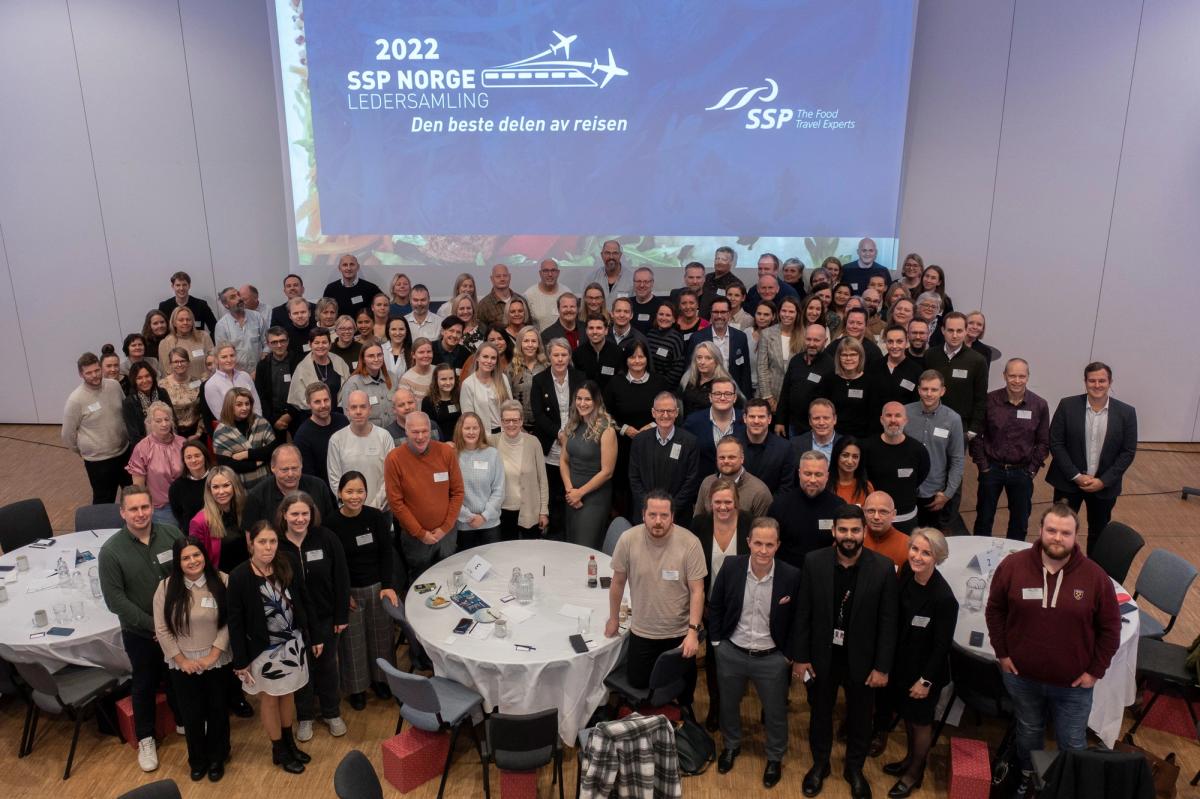 Stor gruppe mennesker i en konferansesal foran en skjerm med «2022 SSP Norge Ledersamling – Den beste delen av reisen»
