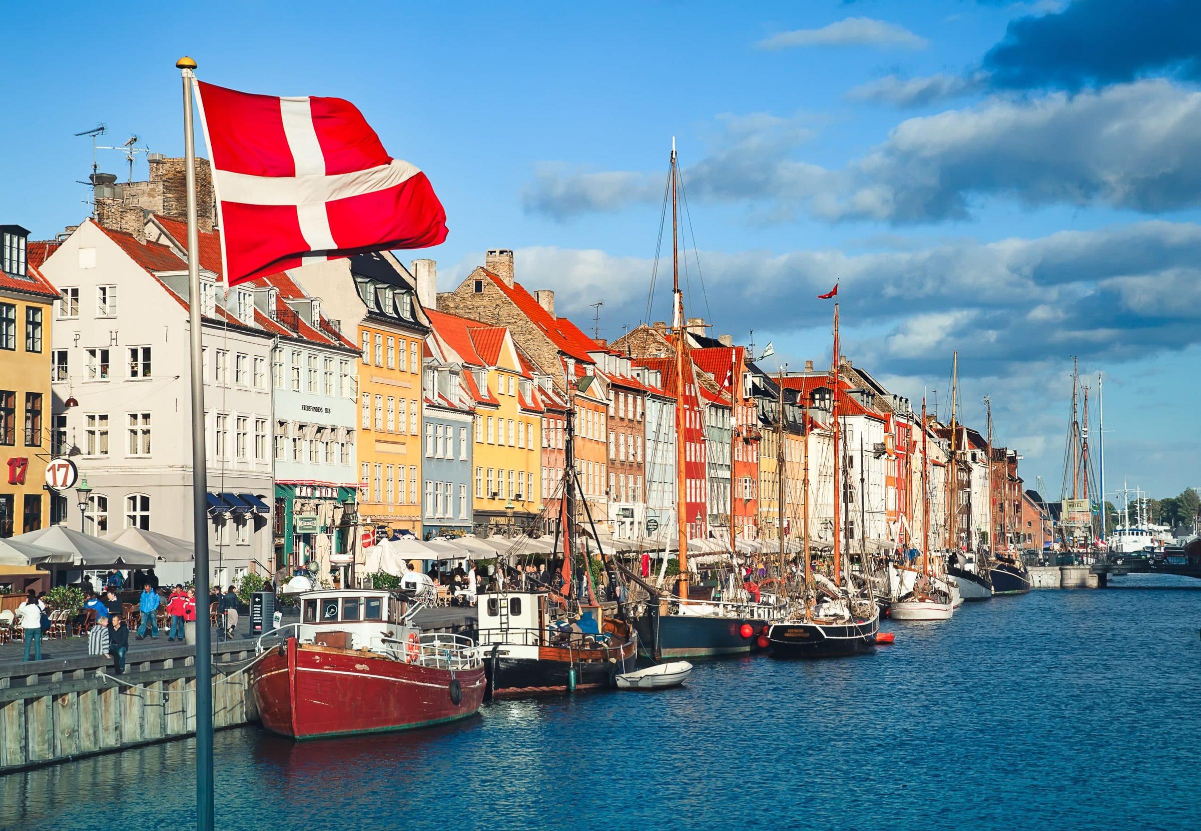 Die dänische Flagge weht über den bunten Stadthäusern und den festgemachten Holzbooten von Nyhavn in Kopenhagen