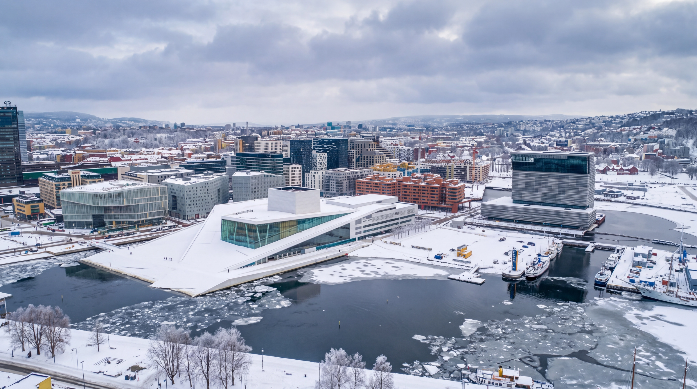 Aerial view of snow-covered Oslo with the Opera House and Munch Museum on a partially frozen waterfront.