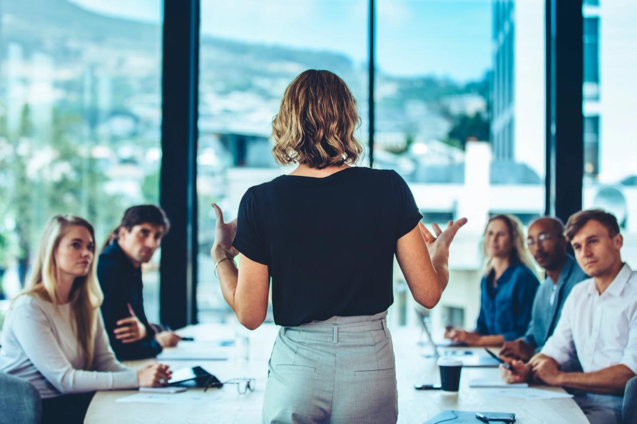Frau präsentiert Kolleginnen und Kollegen an einem Konferenztisch in einem hellen Büro
