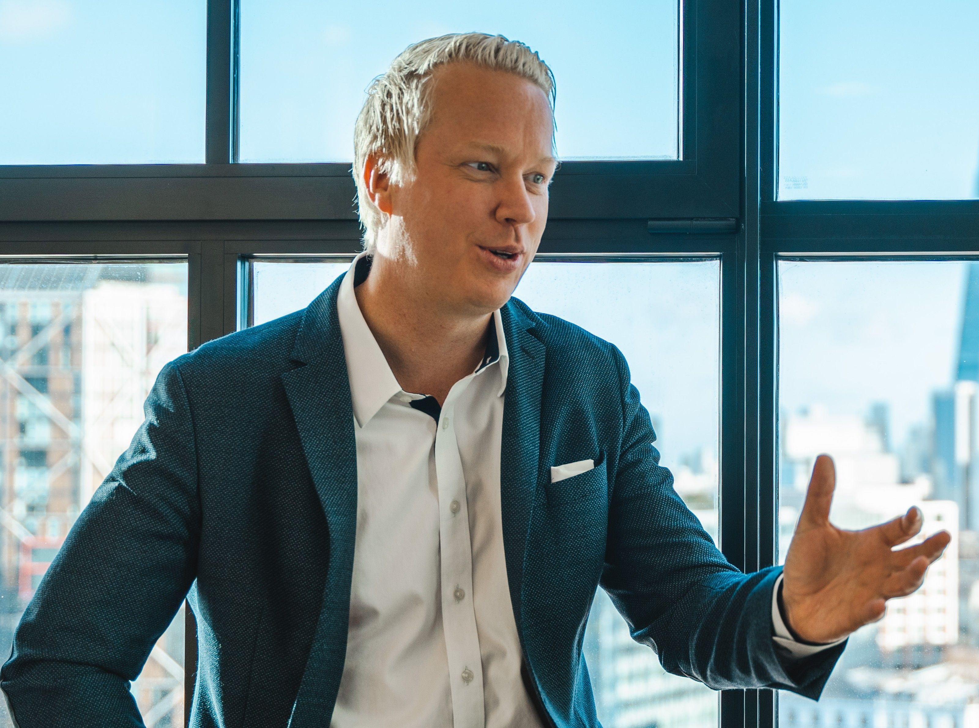 Krister Kristiansen gesturing as he speaks, in a blazer in front of a window with a city view