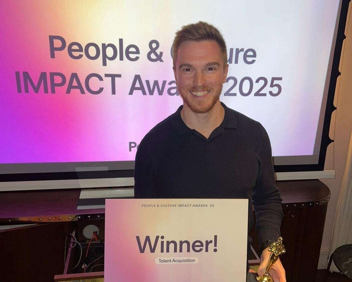 Lächelnder Mann mit einem Winner-Schild für Talent Acquisition bei den People & Culture IMPACT Awards 2025