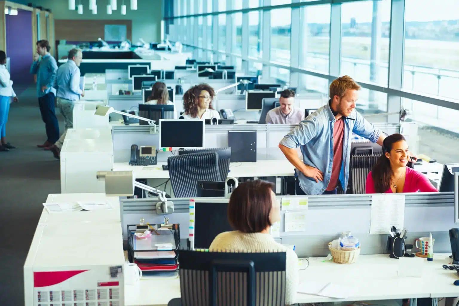 Des collaborateurs travaillent et collaborent dans un bureau moderne en open space aux grandes baies vitrées.