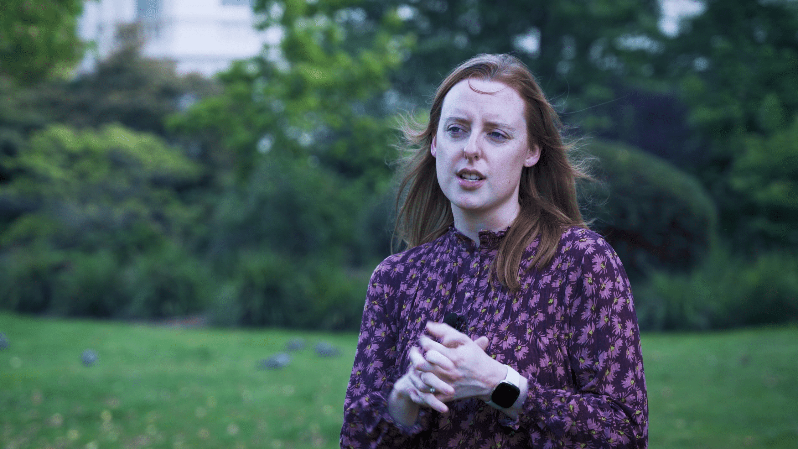 Amy Chandler, eine Frau in einer lila geblümten Bluse, spricht im Freien in einem Park