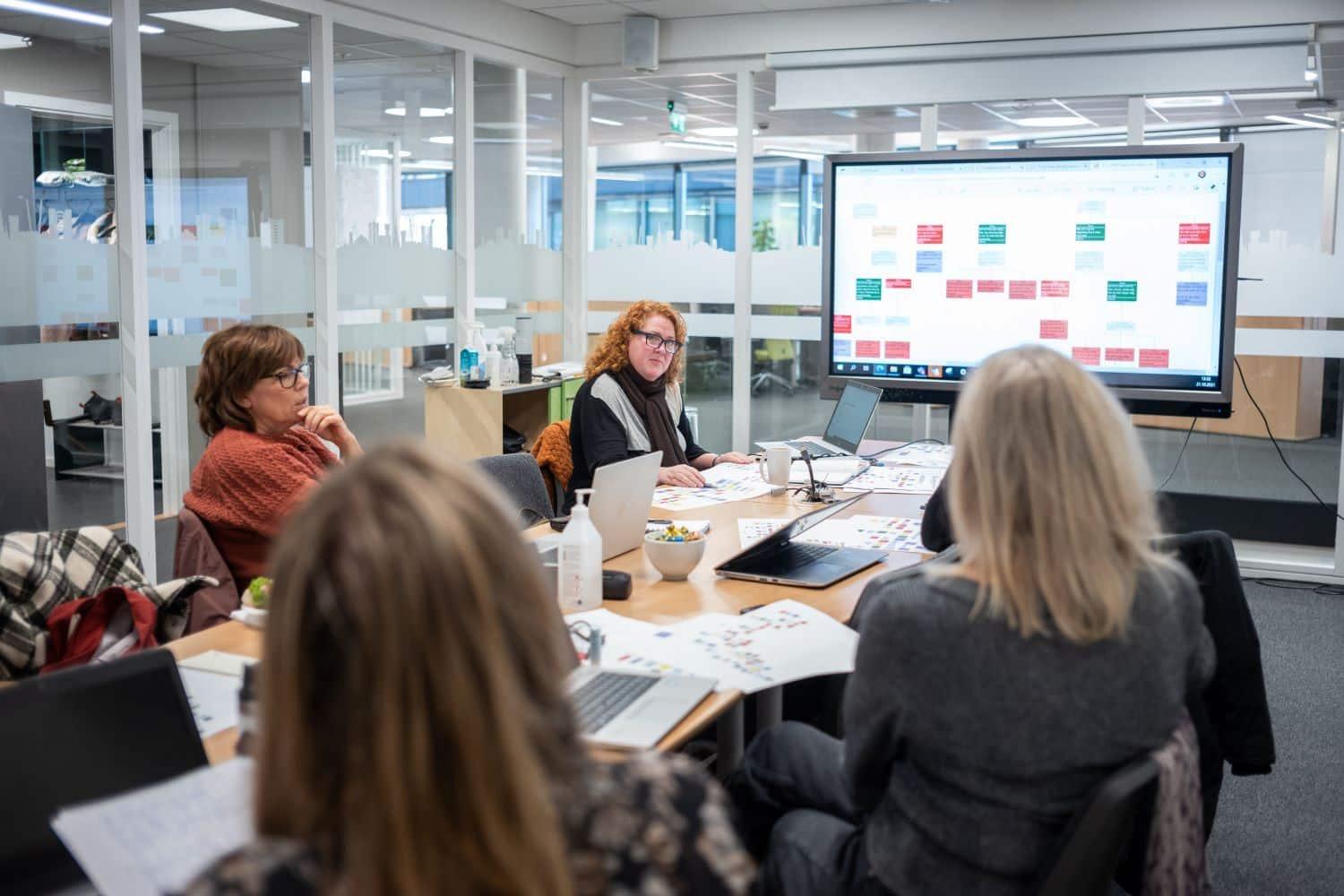 Møte hos Drammen kommune: flere personer rundt et møtebord foran en storskjerm med digital tavle