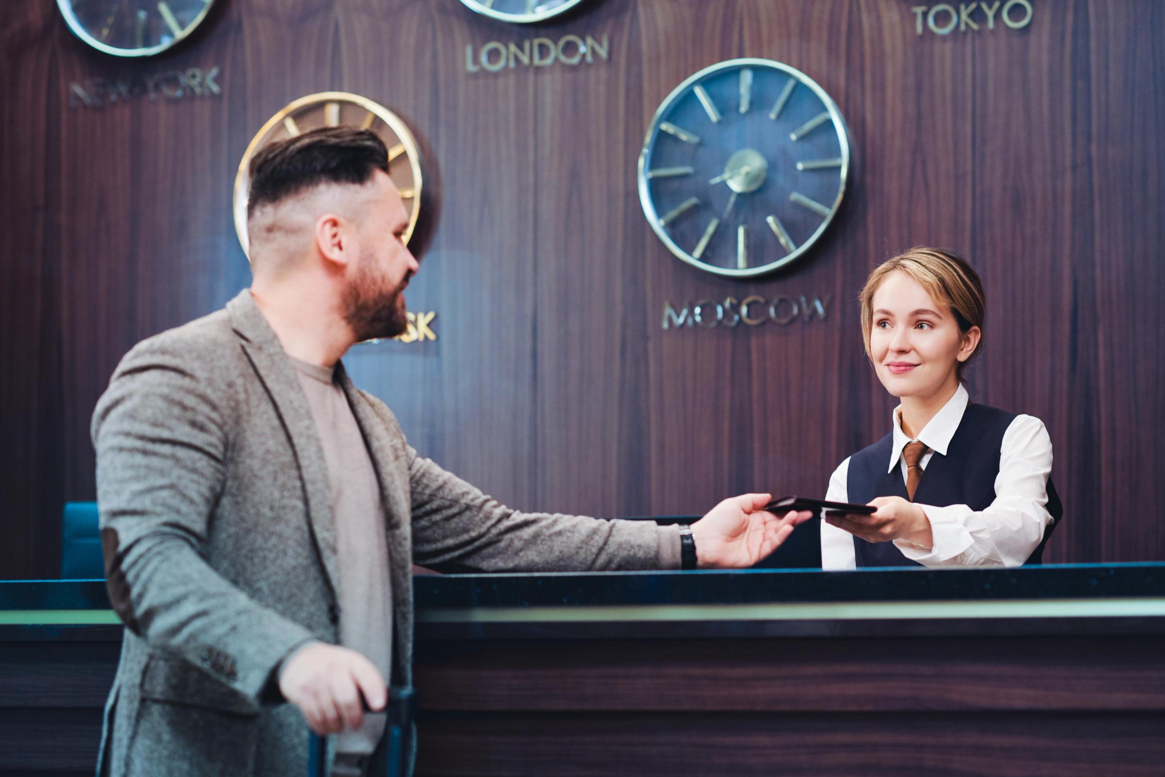 Young female receptionist passing a passport back to a male client after check-in