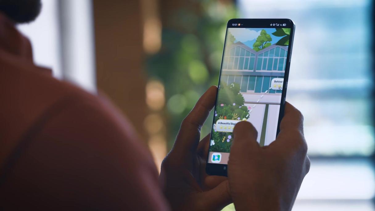 Hands holding a smartphone displaying an augmented reality game with a virtual building and garden.