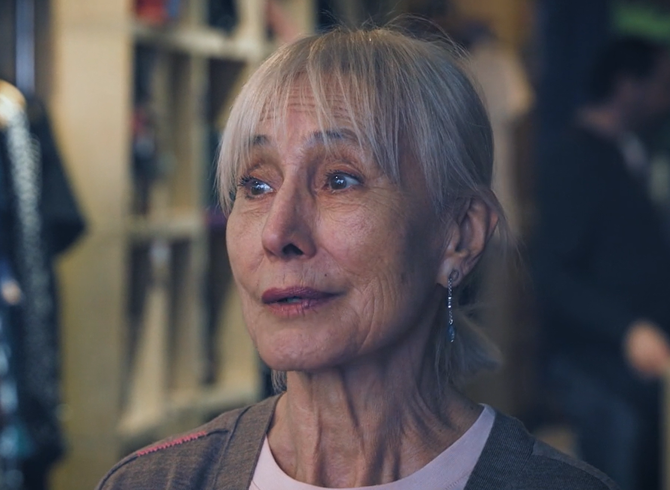 Naza, speaking in a charity shop with shelves and clothing behind her
