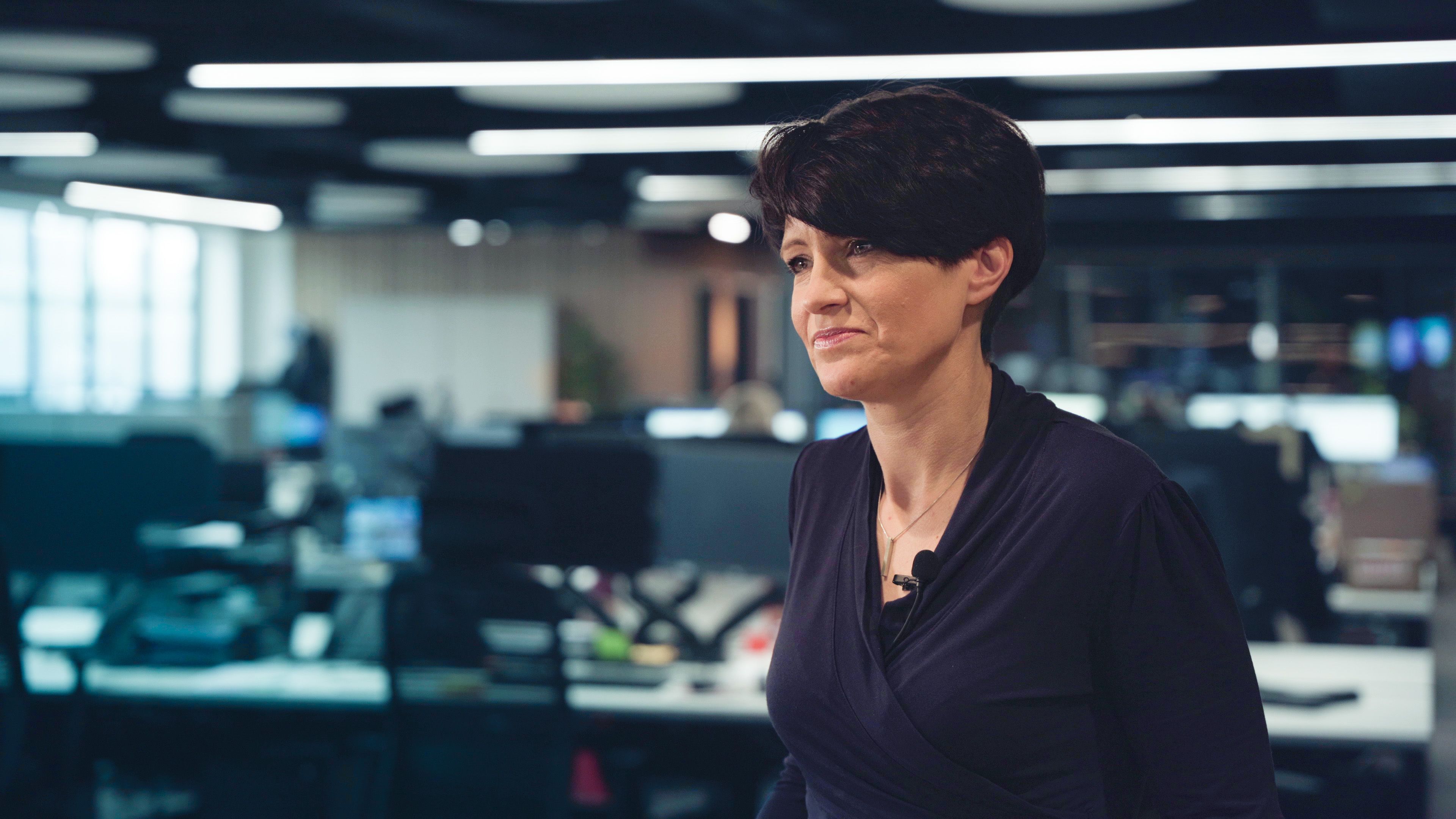 Mel Weatherhead standing in an open-plan office with a clip-on microphone on her top