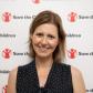 Jen Webb smiling in a polka-dot top in front of a Save the Children branded backdrop