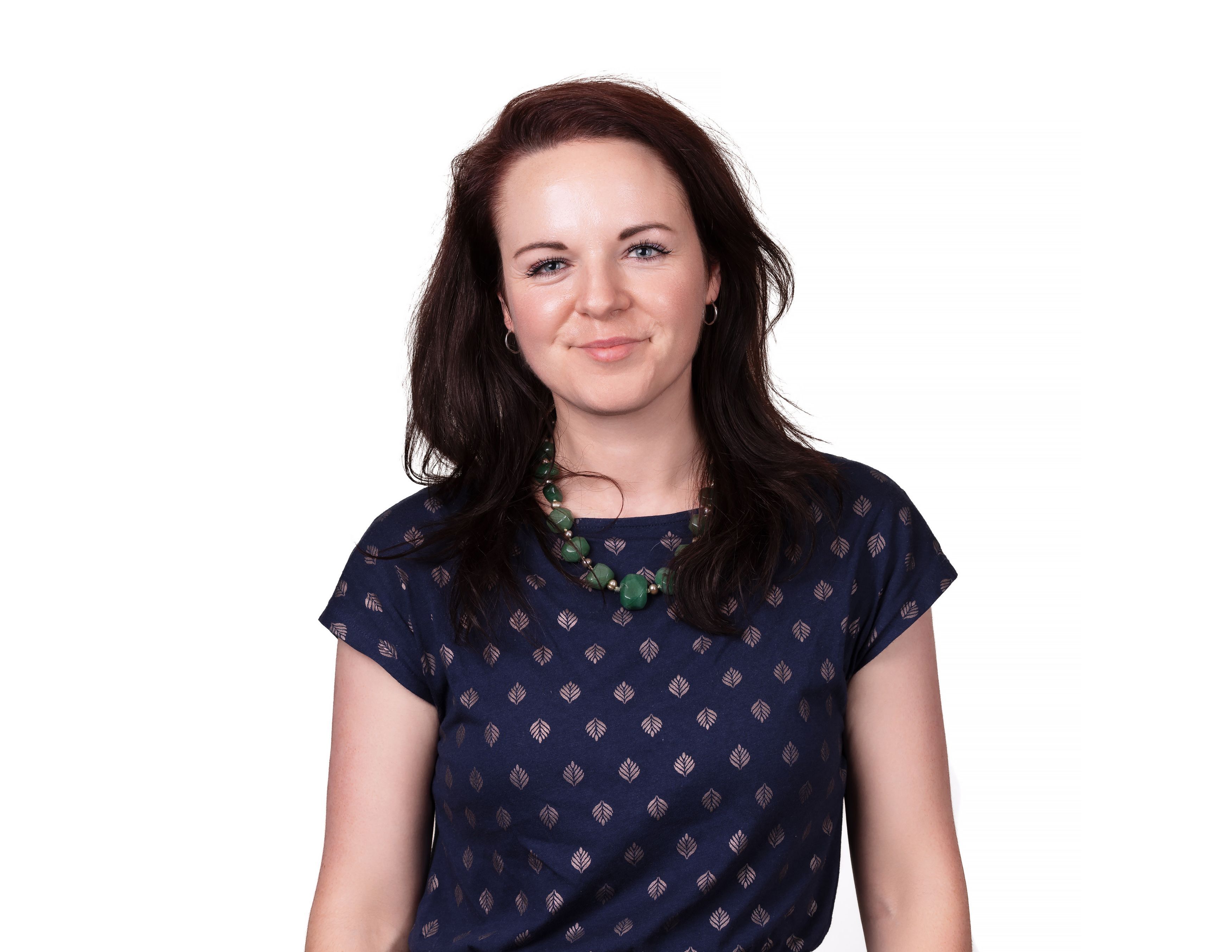 Susie Dunstan in a patterned navy top and green beaded necklace, photographed against white