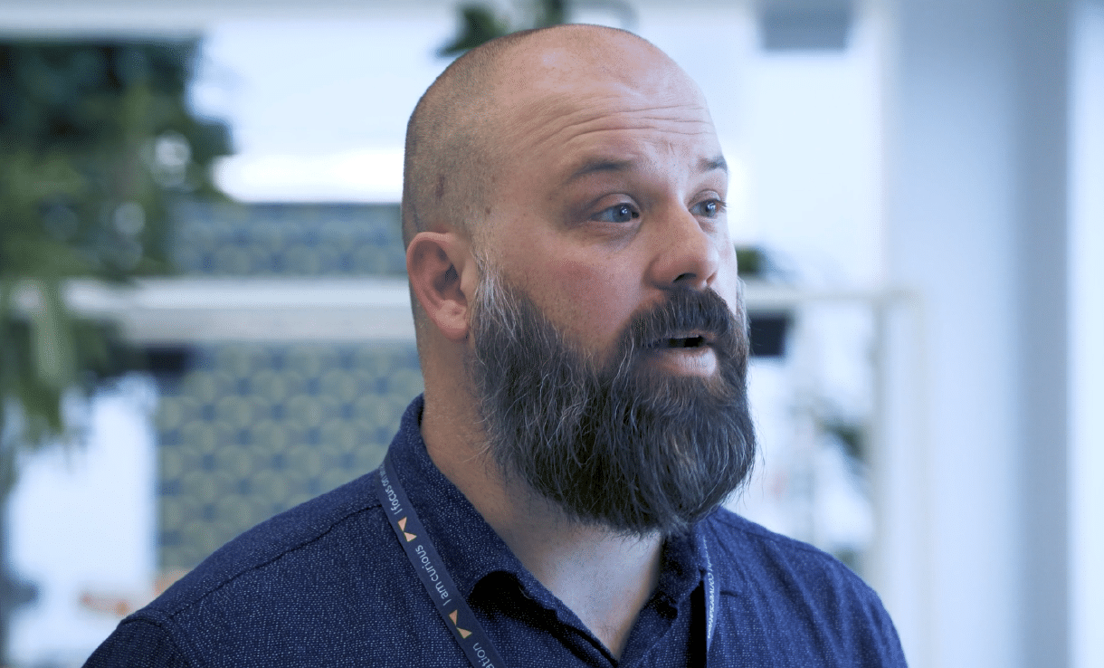 Kevin Bowes, a bearded man wearing a lanyard, talking in a bright office