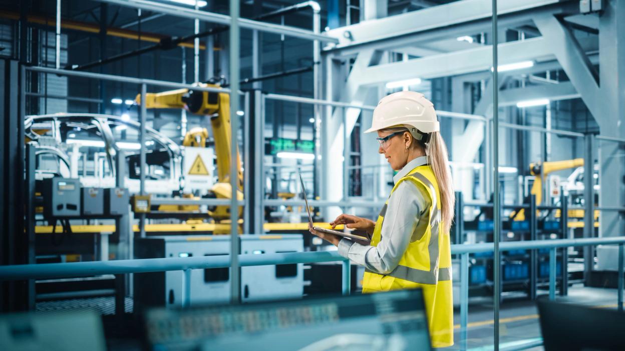 Engineer in a hard hat using a laptop on a factory floor