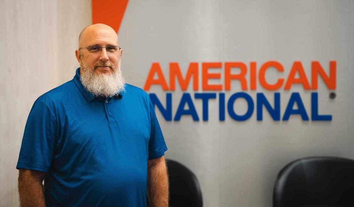 Brandon Freeman in a blue polo shirt standing in front of an American National wall sign