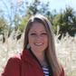 Michelle Kiser smiling in a red jacket, outdoors in front of tall grasses
