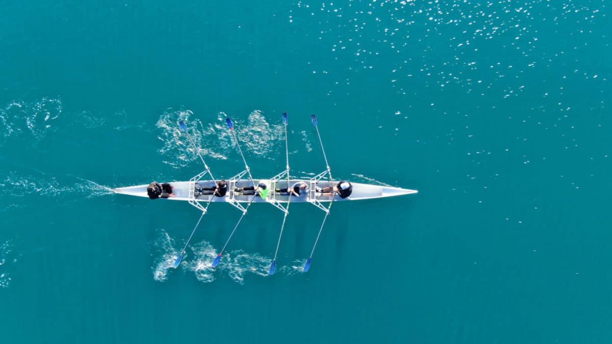 Aerial view of a four-person rowing crew gliding across turquoise water