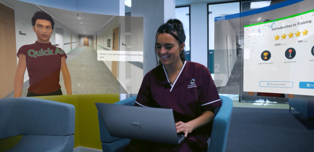 Nurse in burgundy scrubs smiles at a laptop as training screens float beside her