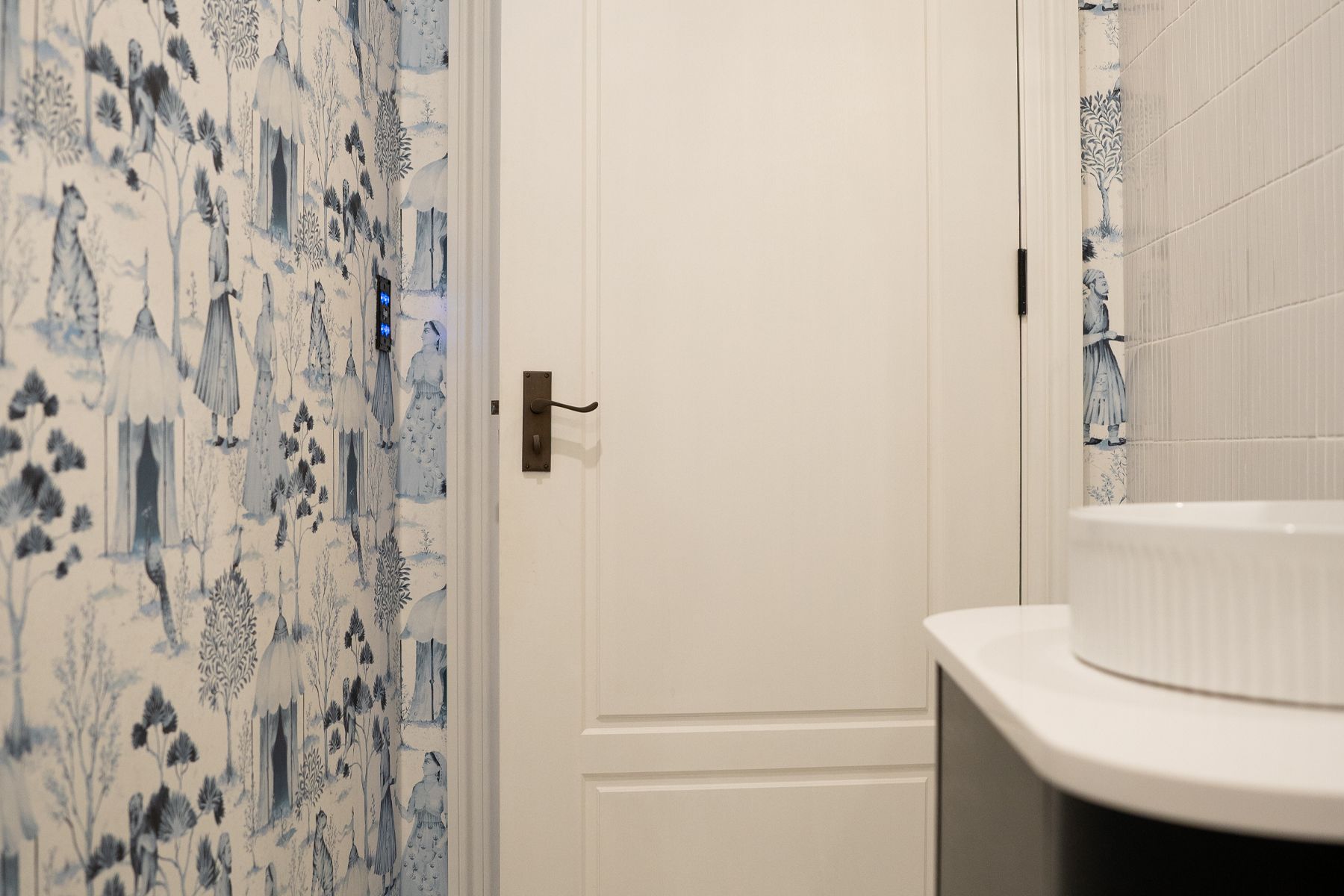 Elegant bathroom with a white Bayview BAY22 panelled door and intricate blue and white patterned wallpaper. A modern white sink with a rippled edge is visible in the foreground.