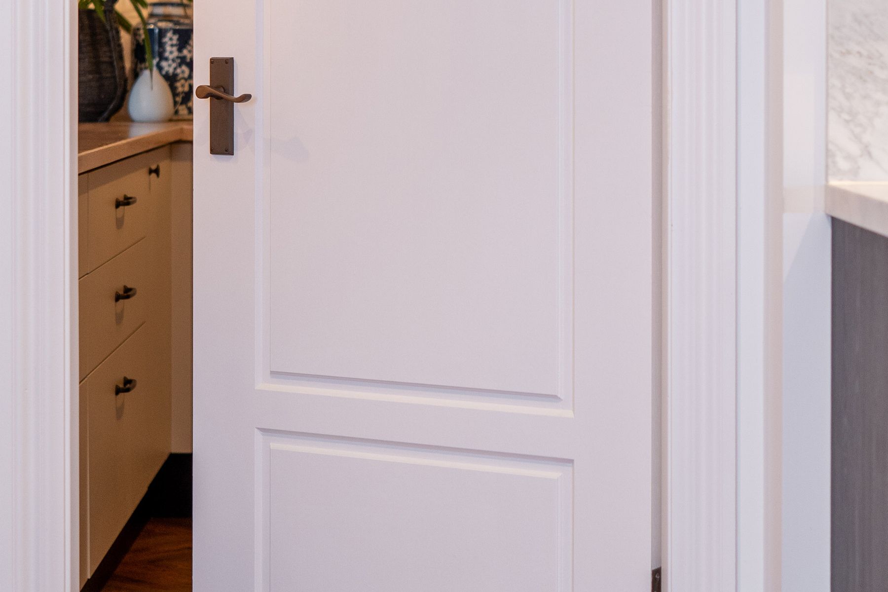 A White Bayview BAY22 door ajar, showing a kitchen with beige cabinets and a wood countertop, soft light, creating a calm and inviting atmosphere.