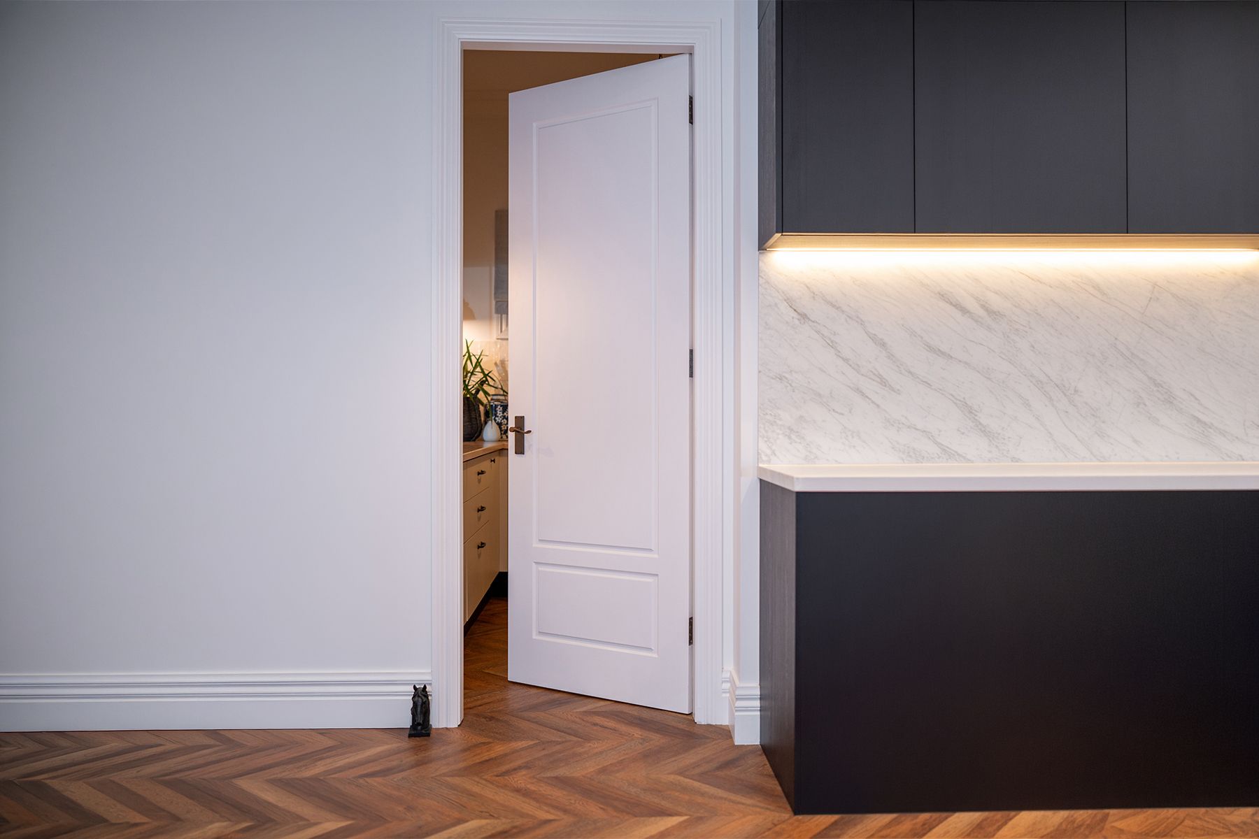 A White Bayview BAY22 door ajar, showing a kitchen with beige cabinets and a wood countertop, soft light, creating a calm and inviting atmosphere.
