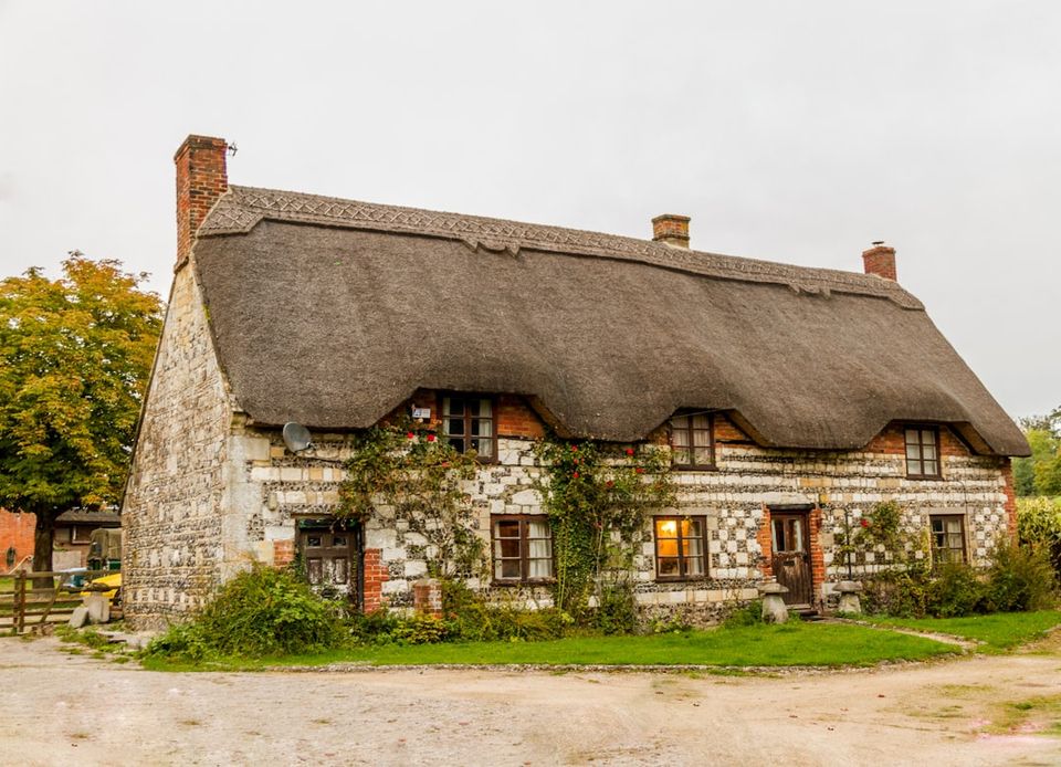 Stone cottage with a thatched roof, ivy-covered walls, and warm windows, evoking a storybook charm reminiscent of hobbit-house design