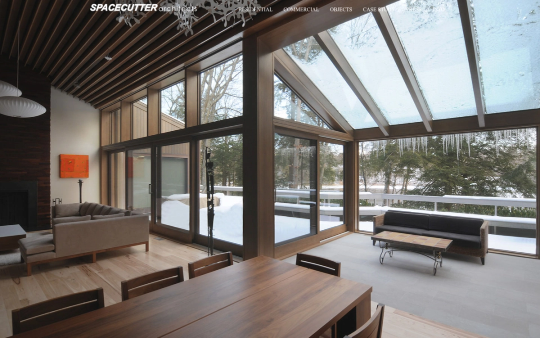 The SPACECUTTER Architects website at spacecutter.com, showing a timber living room under a glazed gable roof over a snowy garden