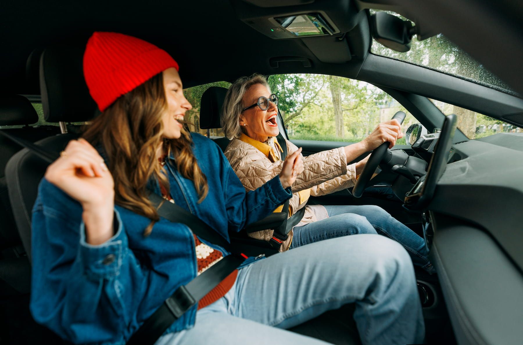 Jüngere und Ältere Frau singen gut gelaunt während sie in einem Auto fahren
