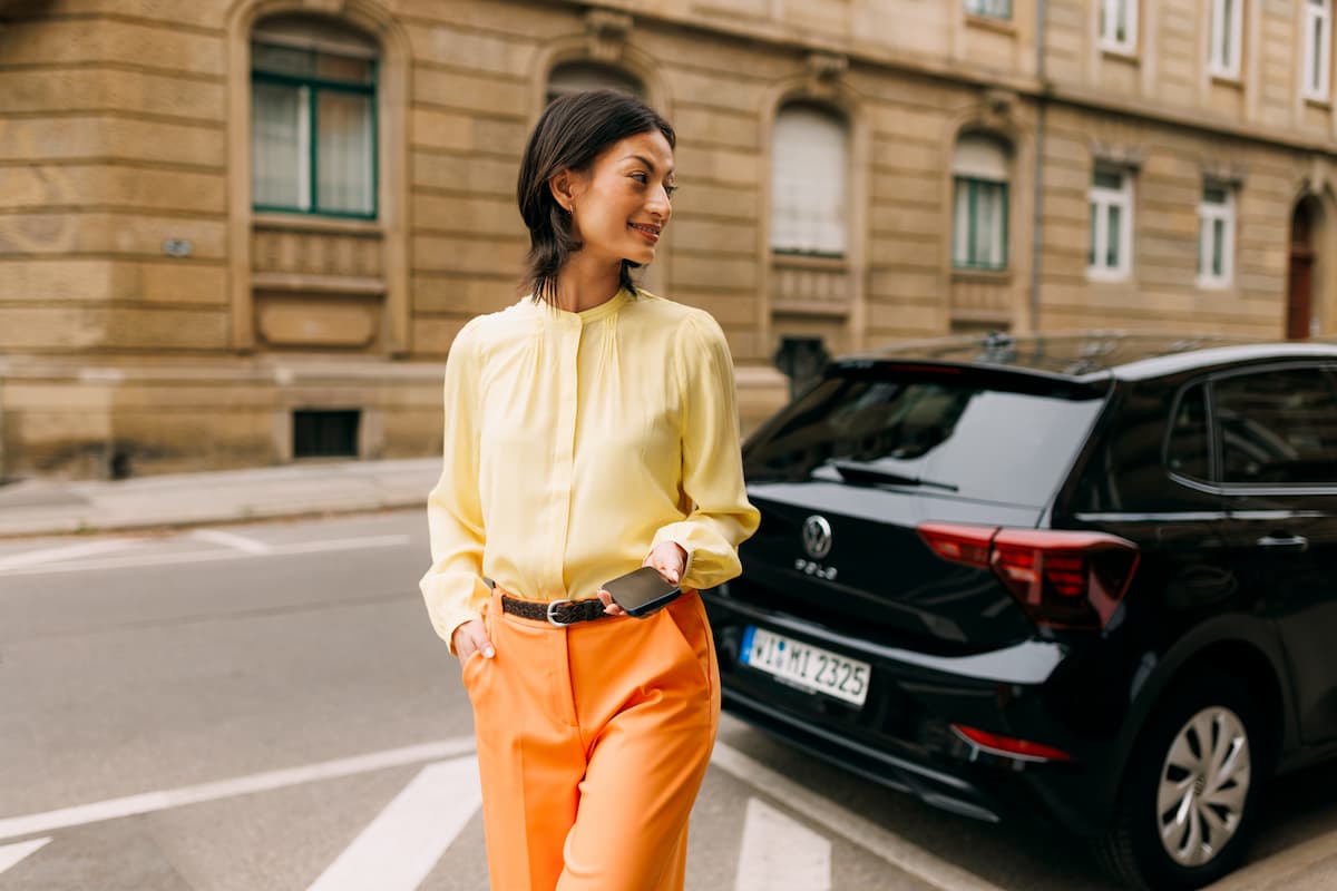 Eine Frau mit Smartphone in der Hand steht neben einem Auto