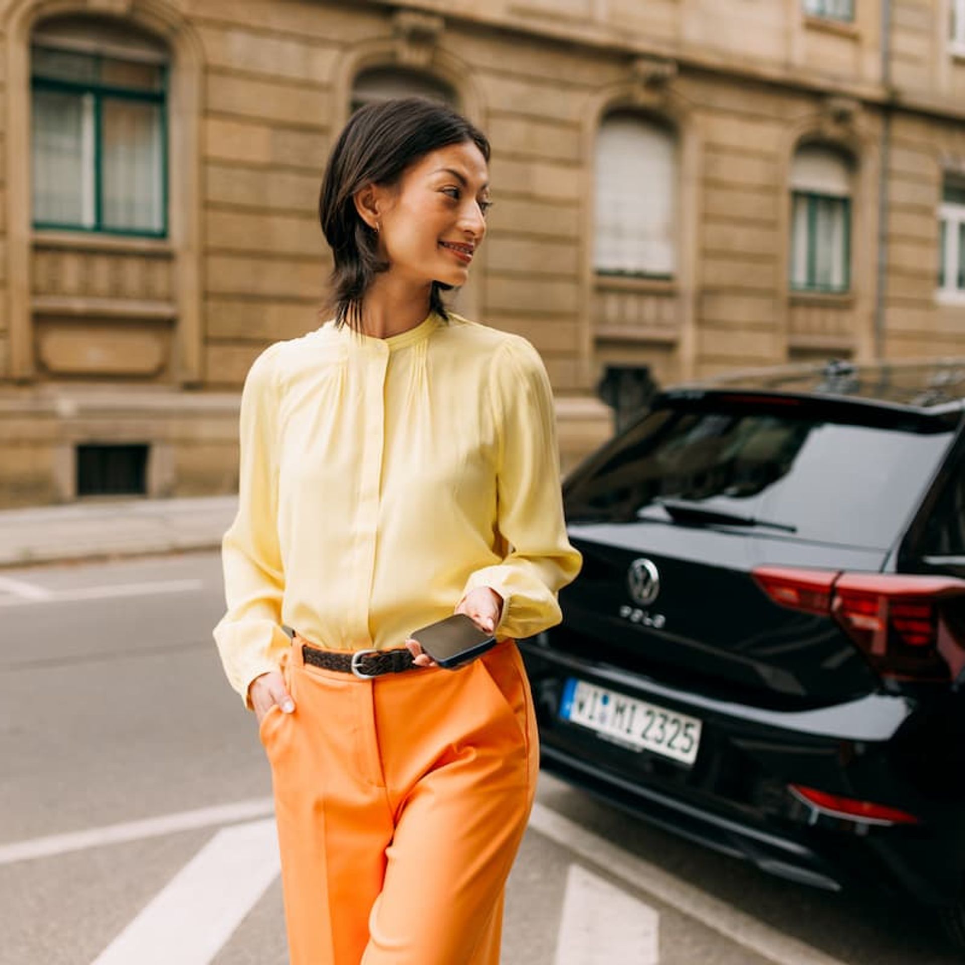 Eine Frau mit Smartphone in der Hand steht neben einem Auto