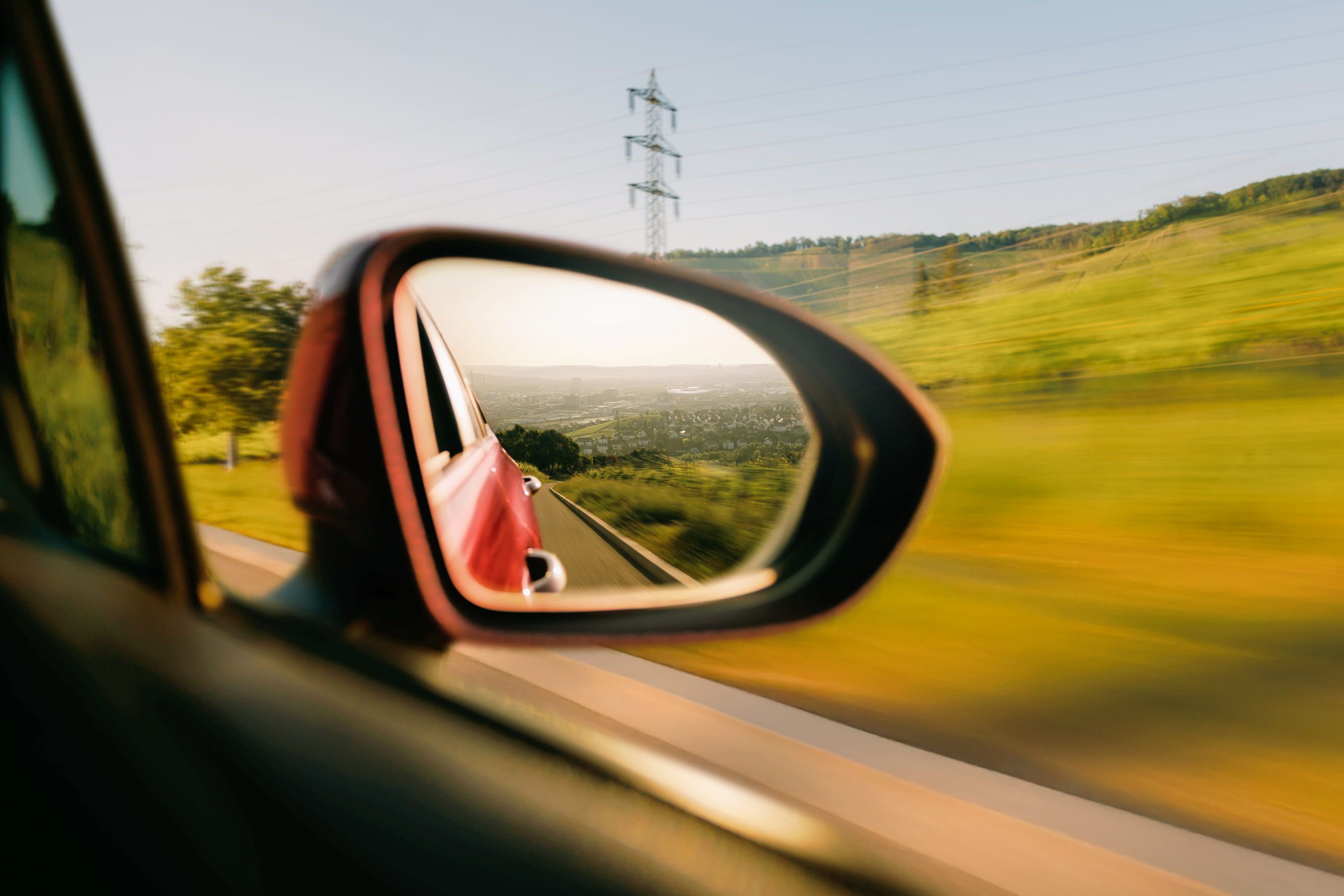 Ein Auto fährt an einer grünen Landschaft vorbei, im Hintergrund ist eine Stadt zu erkennen.