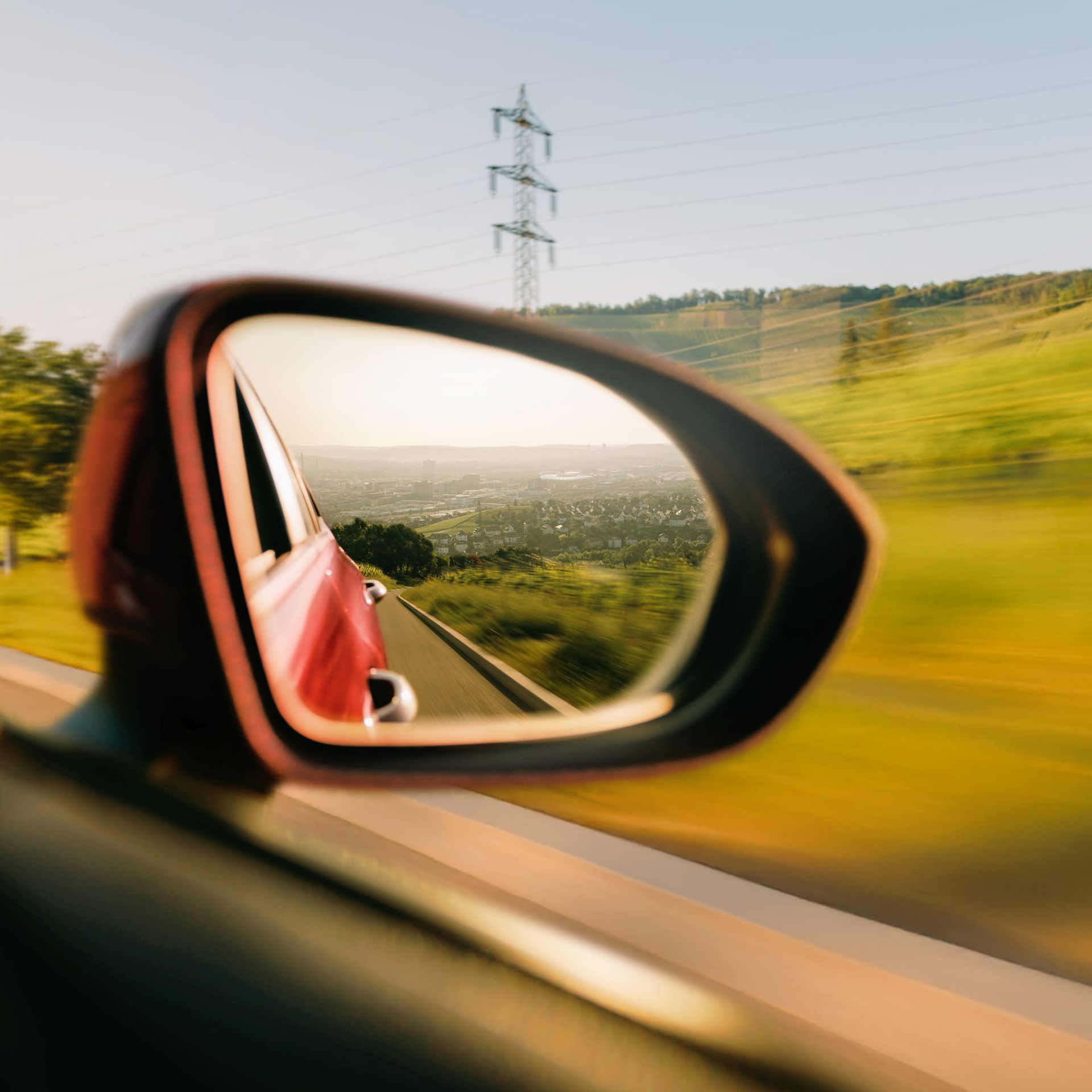 Ein Auto fährt an einer grünen Landschaft vorbei, im Hintergrund ist eine Stadt zu erkennen.