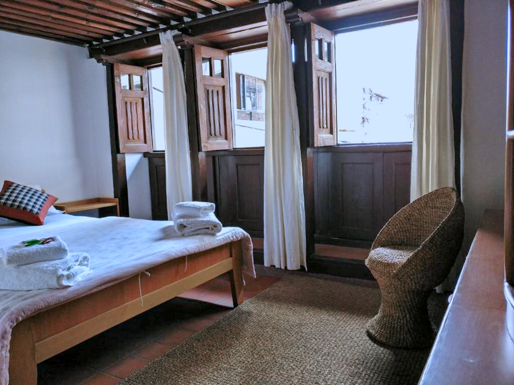 Indrayani double bed beside wooden windows and an armchair
