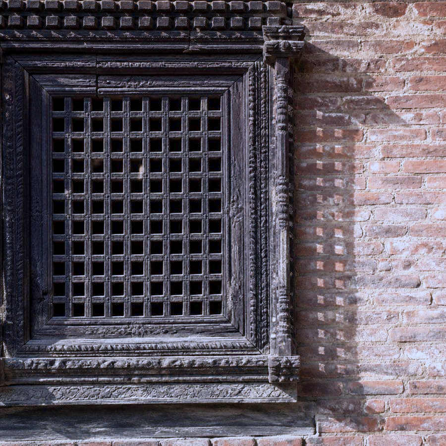 A carved tikijhya lattice window in a brick wall in Patan