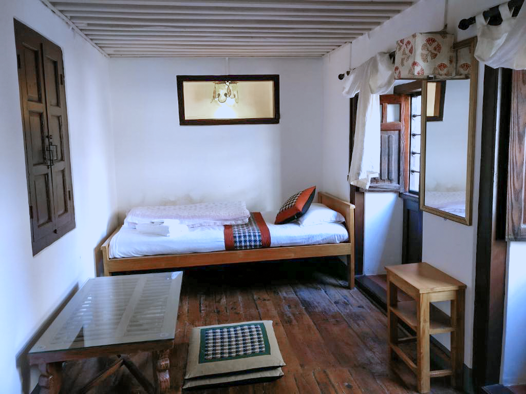 Barahi single bed beside wooden windows and a small table