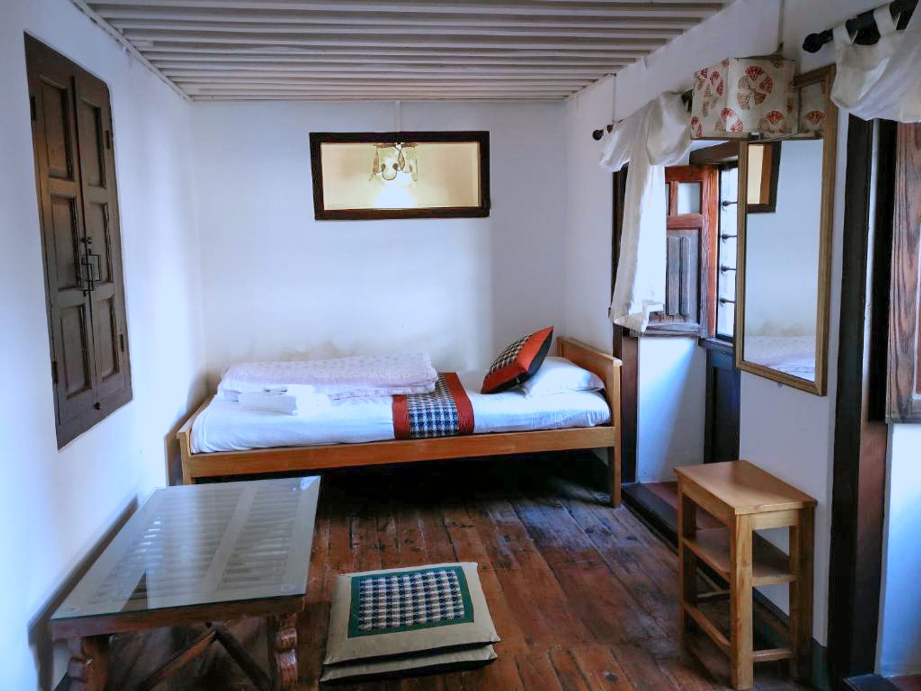 Barahi single bed beside wooden windows and a small table