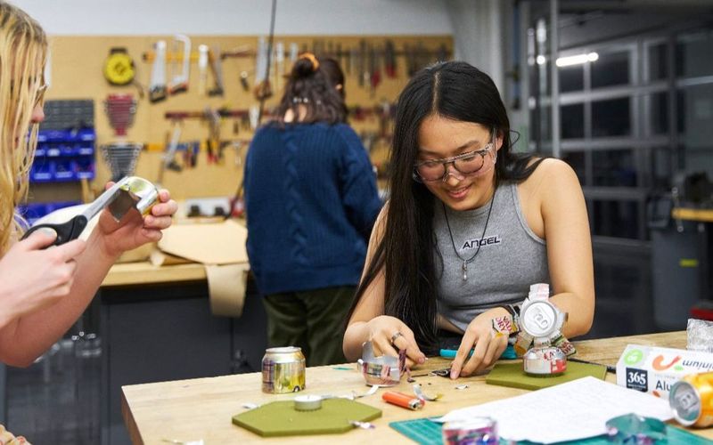 Three students work on projects in the makerspace, smiling and chatting.