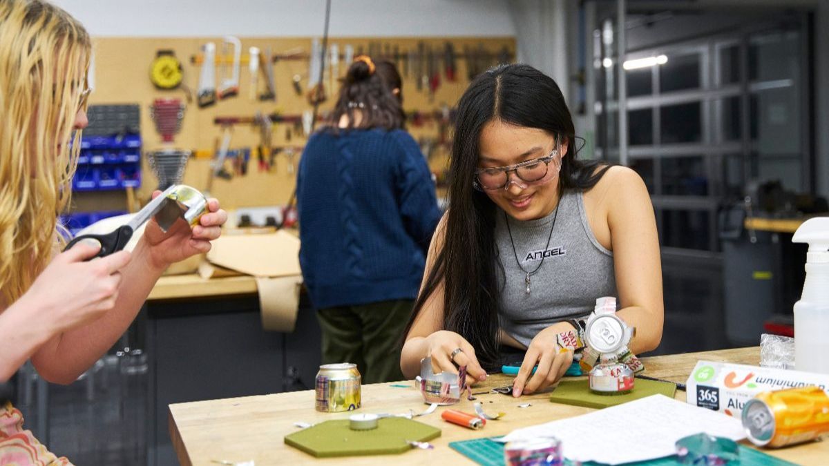 Three students work on projects in the makerspace, smiling and chatting.