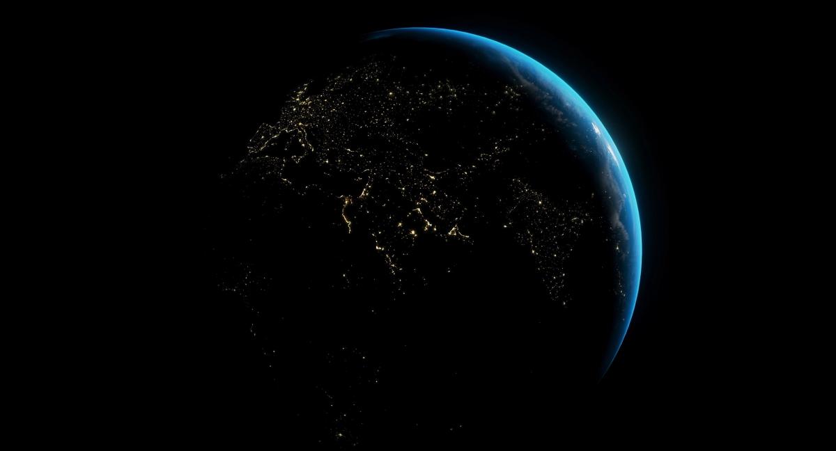 A image of the earth from outerspace. Almost the entire image is black, with a crescent of the earth's ocean being visible. The rest of the earth is in darkness, with the light pollution of cities being clearly visible