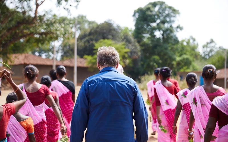 Film still: Patrick Whitney walks away from the camera, surrounded on both sides by people in colorful saris.