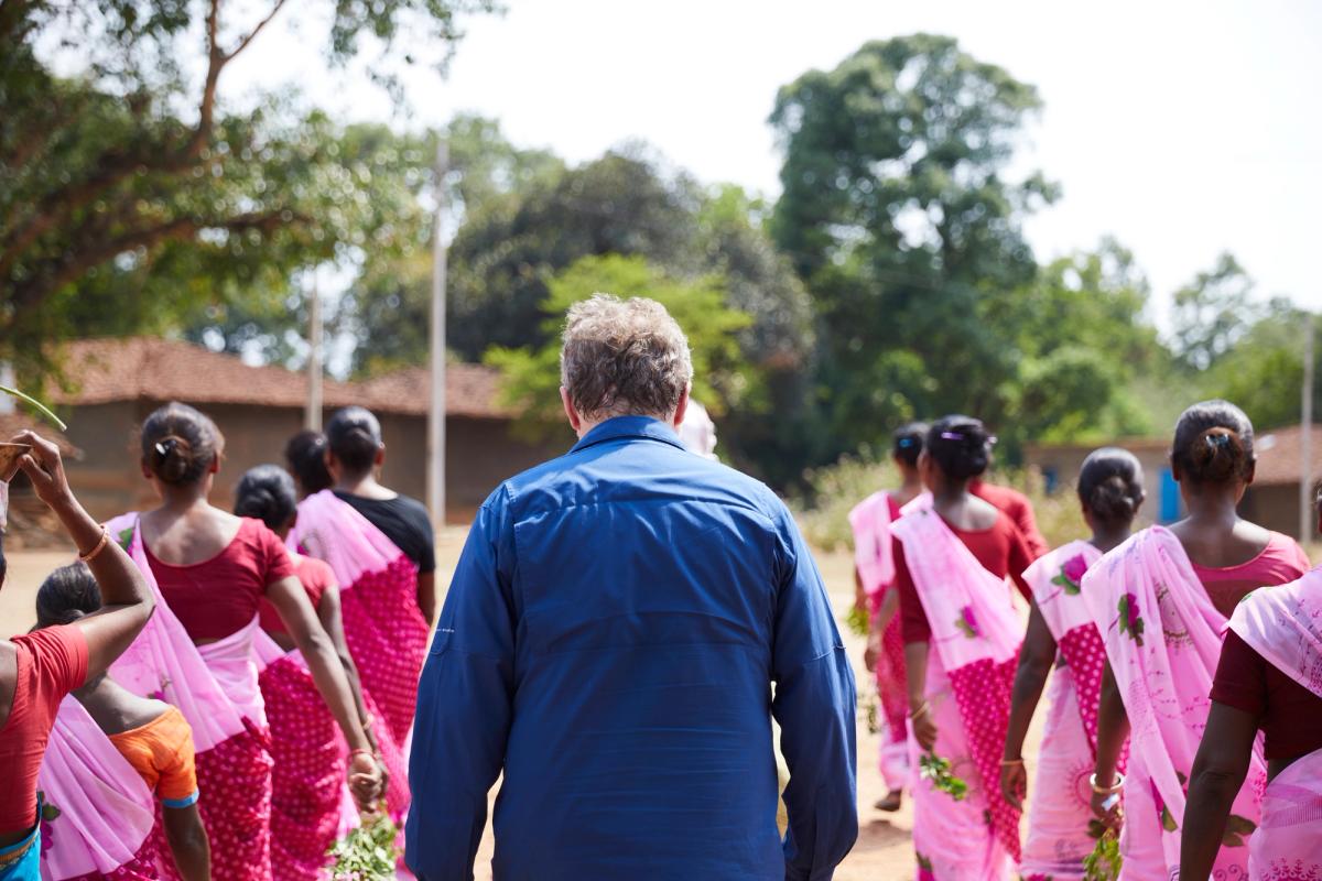 Film still: Patrick Whitney walks away from the camera, surrounded on both sides by people in colorful saris.