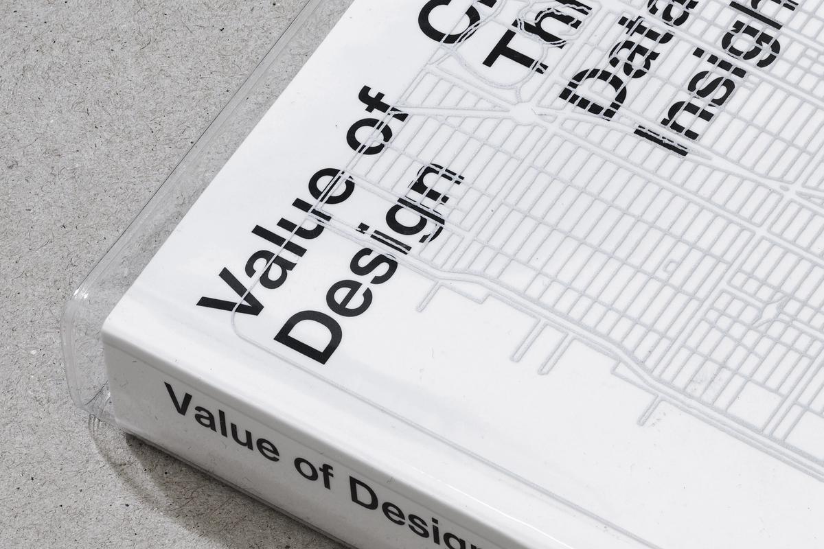 Close-up of the corner of a white book titled Value of Design: Creating Agency Through Data-Driven Insights, resting on a gray concrete surface.