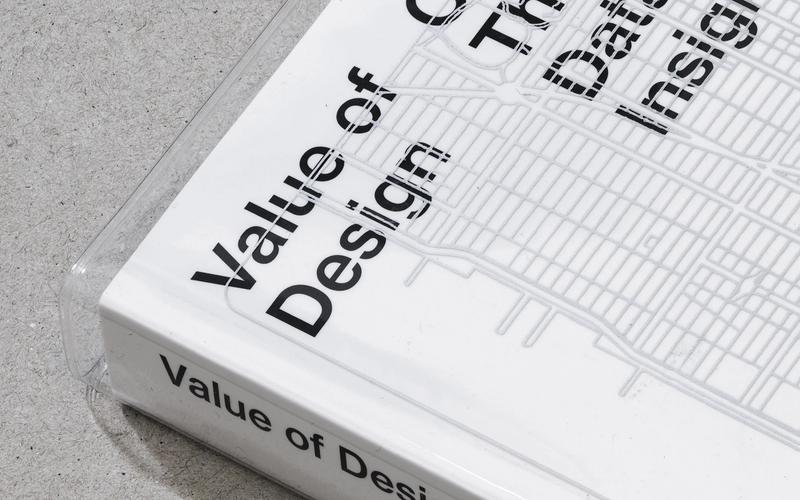Close-up of the corner of a white book titled Value of Design: Creating Agency Through Data-Driven Insights, resting on a gray concrete surface.
