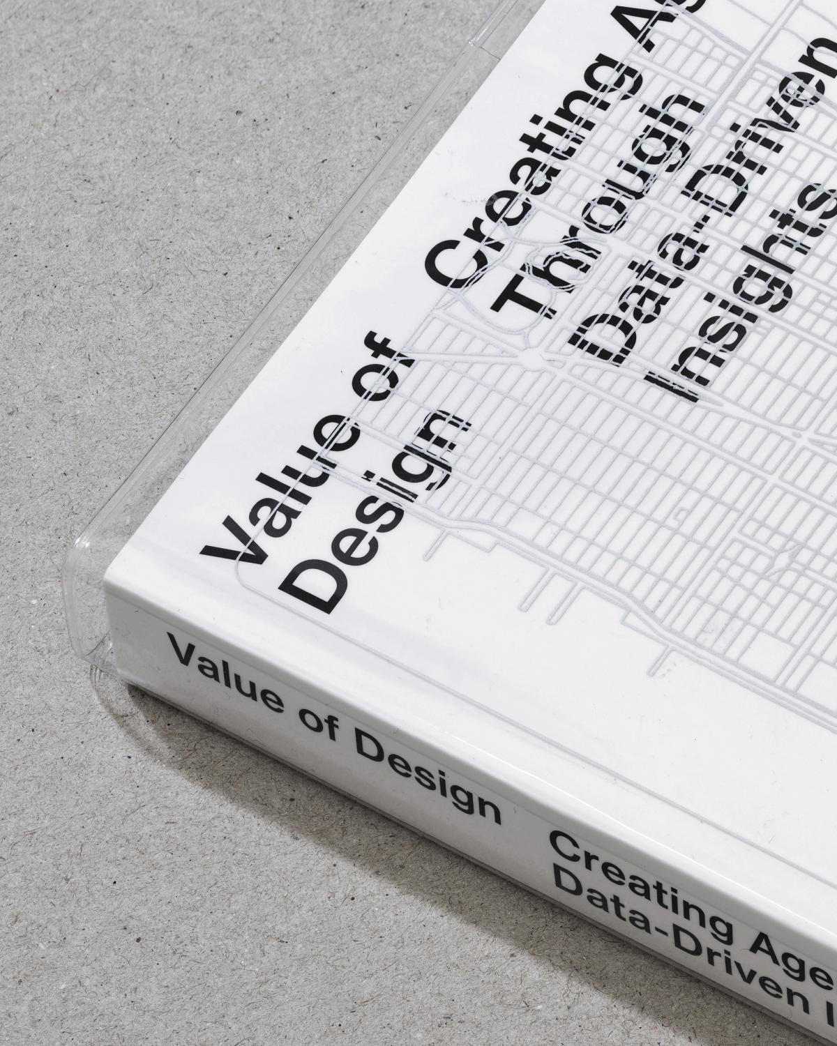 Close-up of the corner of a white book titled Value of Design: Creating Agency Through Data-Driven Insights, resting on a gray concrete surface.