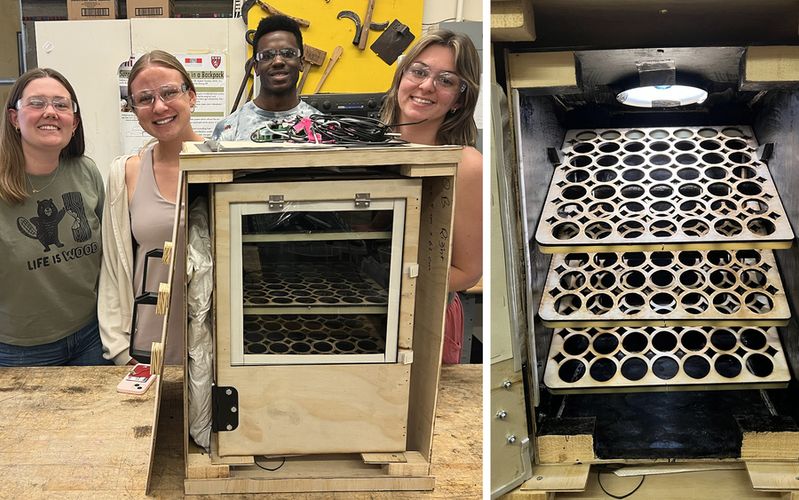Four students pose with a handmade wooden dehydrator featuring a transparent front door and multiple slotted trays inside, designed for drying or processing materials. A close-up on the right shows the interior trays under a heat lamp.