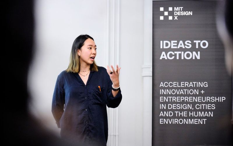 A person presents next to a banner that reads, "MIT DesignX, Ideas to Action."
