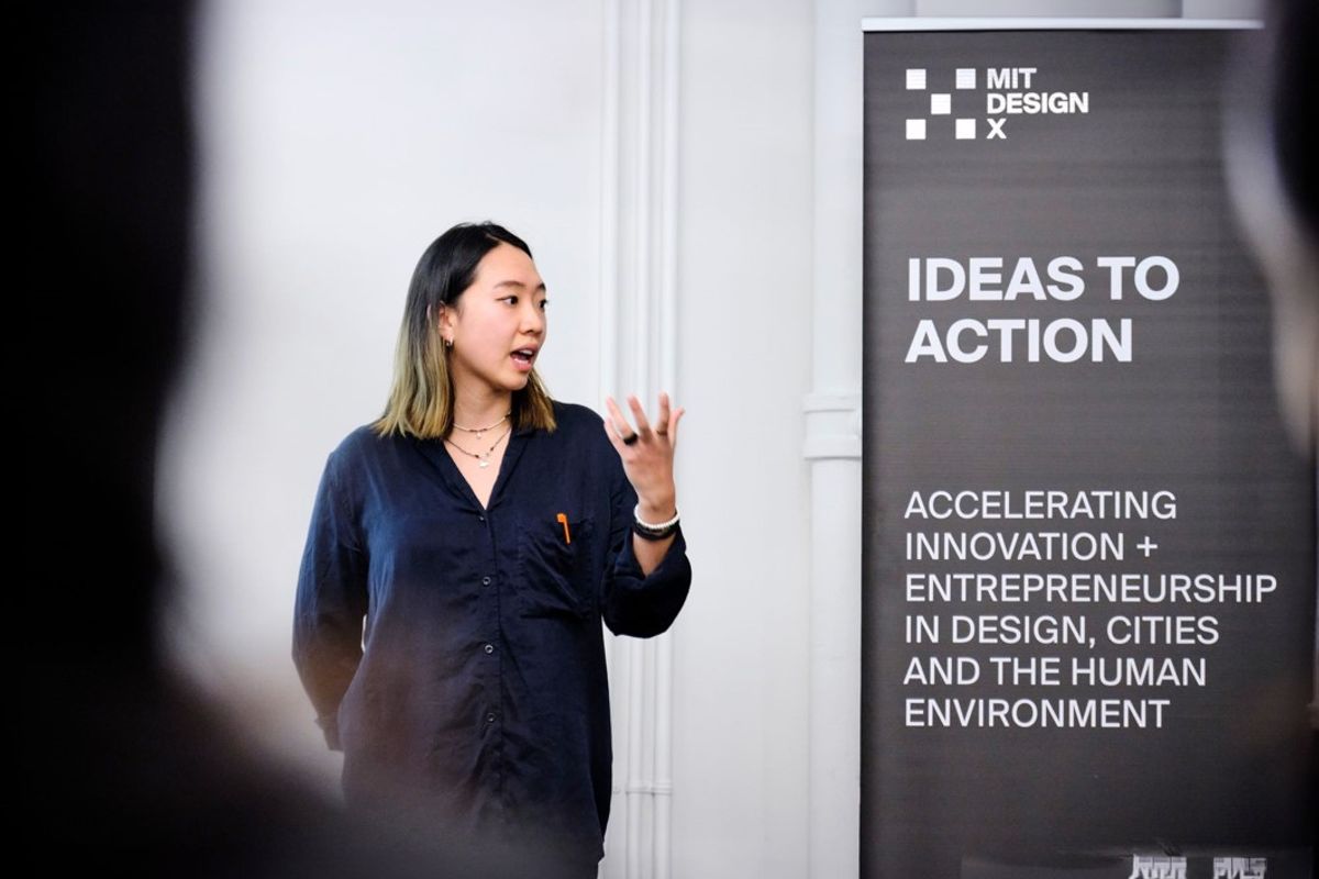 A person presents next to a banner that reads, "MIT DesignX, Ideas to Action."